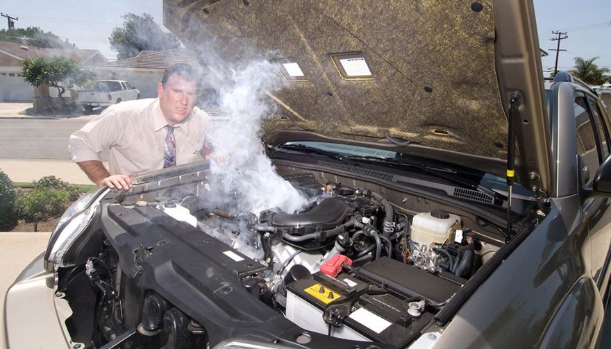 An engine is overheating on the side of the road with steam coming out from under the hood.